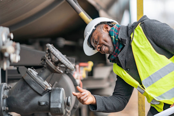 Afro-American train mechanic wearing safety equipment (helmet and jacket) checking and inspecting gear train - Photo, Image