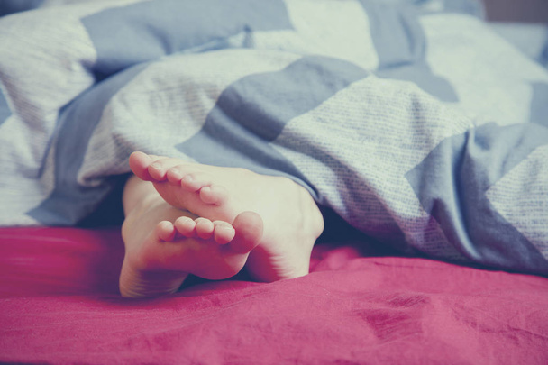 Ноги під ковдрою на ліжку у спальні. Концепція сну та розслаблення
. - Фото, зображення