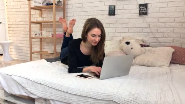 Молодая женщина работает с ноутбуком на кровати. Прекрасная девочка учится дома с помощью компьютера
 - Кадры, видео