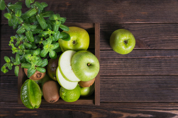 Healthy food background. Concept of healthy food. Fresh green fruits on dark wooden background. Set of green fruits for healthy diet and detox: apple, lime, kiwi, mango, carambola and mint. Overhead - Φωτογραφία, εικόνα