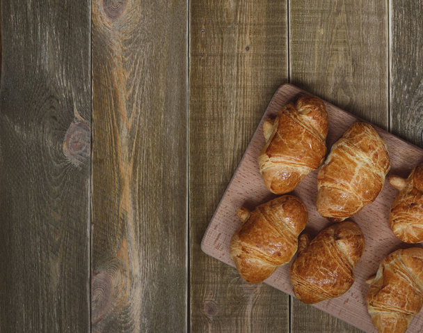 čerstvě upečený domácí croissanty se zlatou kůrkou na hnědý rustikální dřevěný stůl. pohled shora. prostor pro text - Fotografie, Obrázek