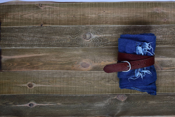 Widok z góry Wysoka talia kobiet niebieski składany dżinsy i skórzany pasek na brązowym tle drewnianych. koncepcja Nastolatki. nastolatek. - Zdjęcie, obraz