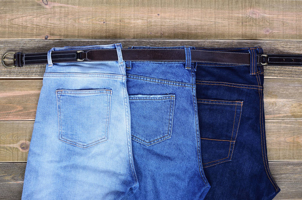 team building. family. three pairs of high waist jeans are connected together by one strap on brown wooden background - Photo, Image