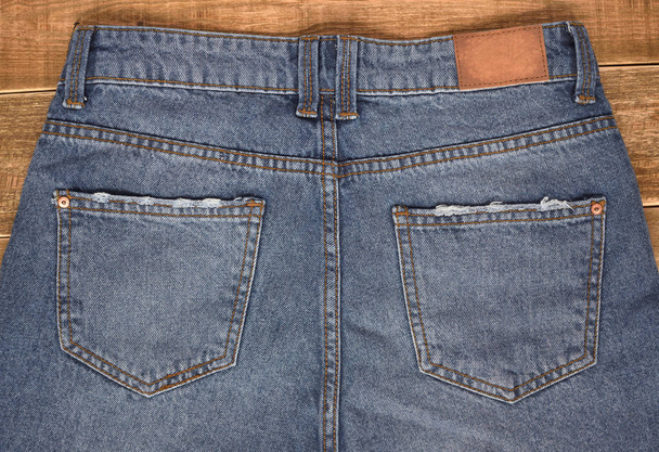 Draufsicht auf High Taille Jeans Rückansicht auf braunem Holzhintergrund. Nahaufnahme Jeans Gesäßtaschen. Teenager-Hintergrund. - Foto, Bild