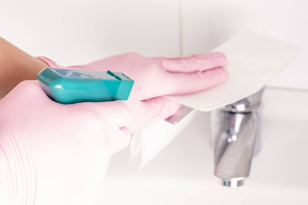 Uma mulher lava suas luvas rosa com uma pia branca e uma torneira no banheiro em casa com guardanapos e spray. Limpeza para brilhar com prazer
 - Foto, Imagem