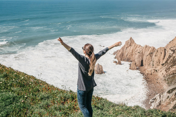 Tyttö Atlantin valtameren rannalla Portugalissa nostaa kätensä ylös osoittaa, kuinka tyytyväinen hän on
 - Valokuva, kuva