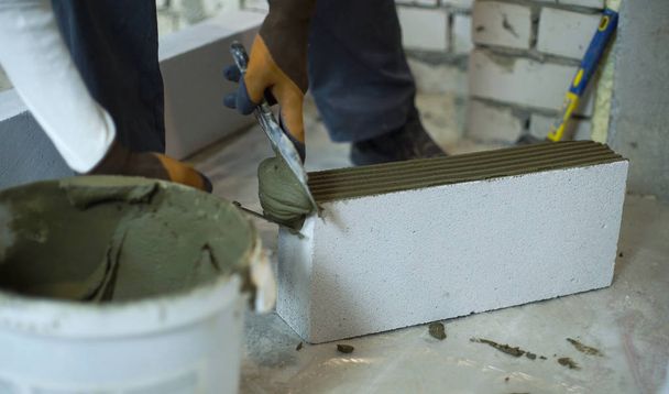 builder putting mortar on sides of aerated concrete block with spatula - Photo, Image