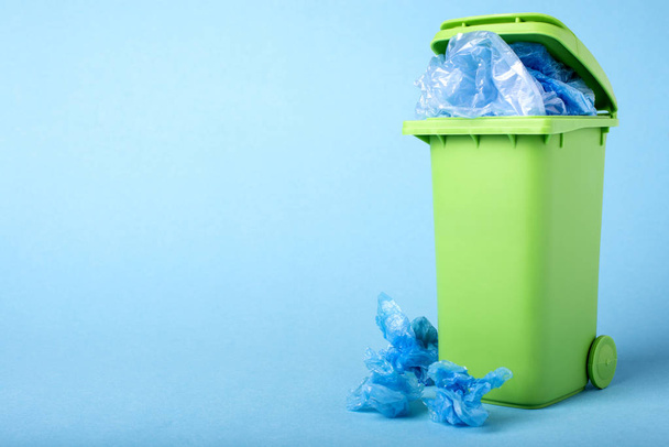 Green dustbin on a blue background. Polyethylene. Recycling. Materials for recycling and reuse on a blue background. Ecological concept, many recyclable objects in container - Photo, image