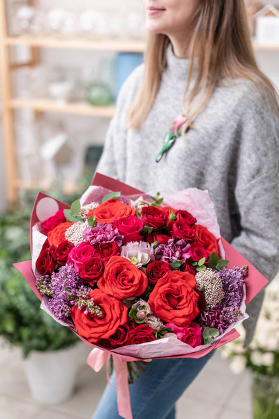 beautiful fresh cut bouquet of mixed flowers in woman hand. the work of the florist at a flower shop. Red color - Photo, Image