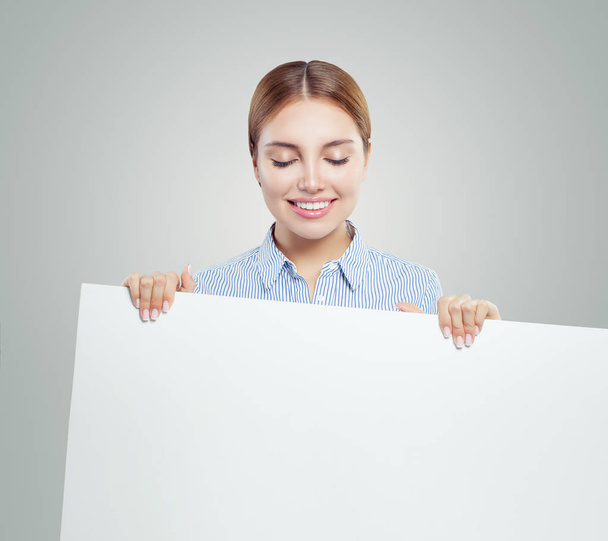 Jovem mulher sorrindo mostrando branco banner papel vazio fundo com espaço de cópia. Retrato de mulher feliz, conceito de negócios e educação
 - Foto, Imagem