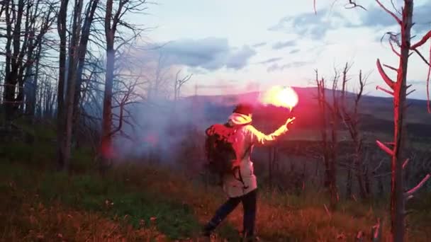 Serious young woman standing alone on the cliff with red smoke bomb and enjoy the beautiful natural scene in day light opening her eyes. Autumn green forest and blue mountains under the cloudy sky - Footage, Video