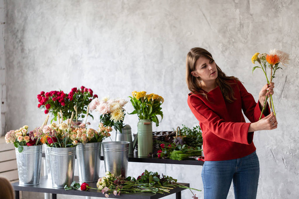 Floristik-Arbeitsplatz. Frau arrangiert einen Strauß mit Rosen, Chrysanthemen, Nelken und anderen Blumen. Floristiklehrerin in Meisterkursen oder Kursen - Foto, Bild