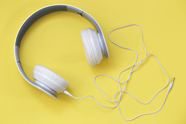 λευκά ακουστικά σε κίτρινο φόντο. Μουσική αντίληψη. Ακουστικά σε κίτρινο φόντο. - Φωτογραφία, εικόνα