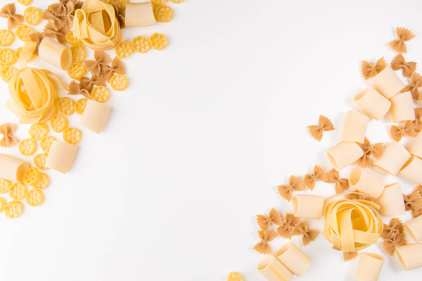An overhead photo of different types of pasta, including spaghetti, penne, fusilli, and others, flay lay on a white background with a place for text - Foto, afbeelding