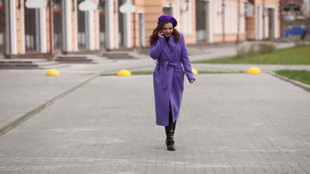 紫色のコートとベレー帽の通りに電話で話しているのスタイリッシュな女性. - 映像、動画