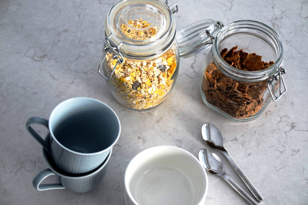 ブルーのマグカップ、白いボウル、スプーンや穀物の瓶と朝食のテーブル - 写真・画像