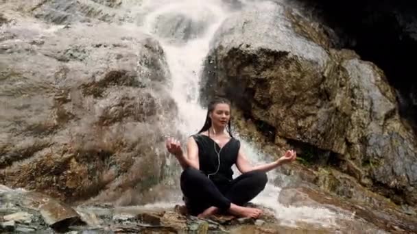 Kobieta robi joga na kamieniu w pobliżu z wodospadem - Materiał filmowy, wideo