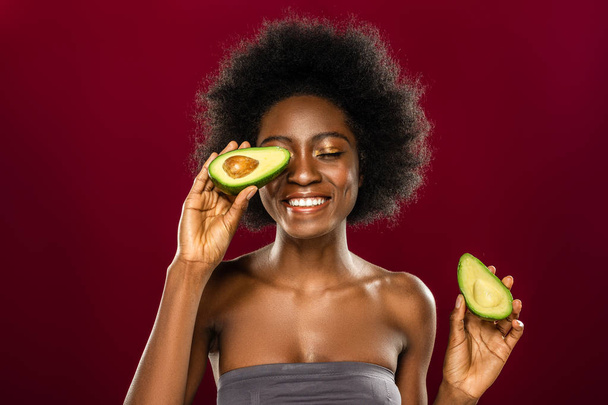Positive happy woman putting an avocado half to her eye - Zdjęcie, obraz