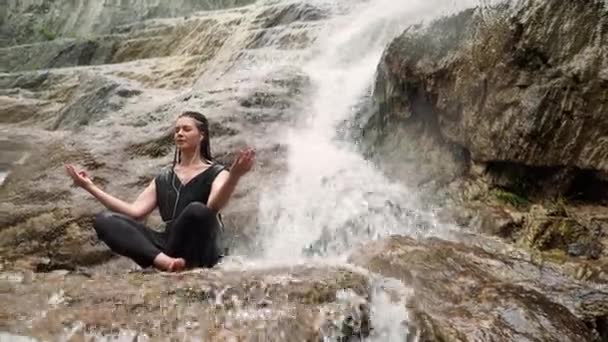 滝の近くの石の上のヨガを行う女性 - 映像、動画