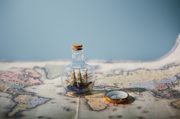 Selective focus of toy ship in glass bottle, map and compass with copy space isolated on blue  - Φωτογραφία, εικόνα