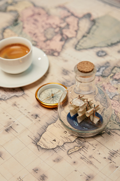 selective focus of coffee cup, compass and toy ship in glass bottle on map - Φωτογραφία, εικόνα