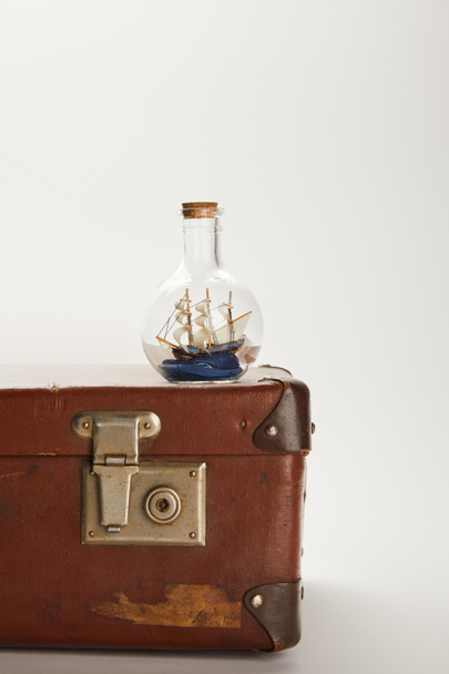 Spielzeugschiff in Glasflasche auf braunem Koffer mit Kopierraum  - Foto, Bild