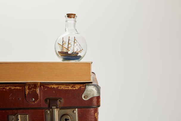 toy ship in glass bottle and book on brown suitcase with copy space  - Valokuva, kuva
