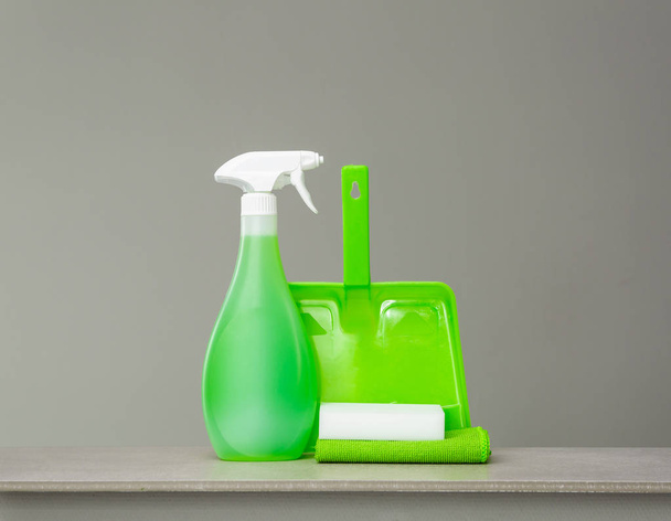 Cleaning green spray bottle with plastic dispenser, sponge, scoop and dust cloth on grey background. Cleaning tools. - Photo, image