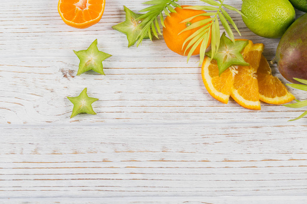 Groene palmbladeren en verse tropische segmenten van vruchten op witte houten tafel. Sappige sinaasappelen, mandarijnen, limoenen, carambolas. Zomer fruit achtergrond. Plat lag, top uitzicht, kopie ruimte - Foto, afbeelding