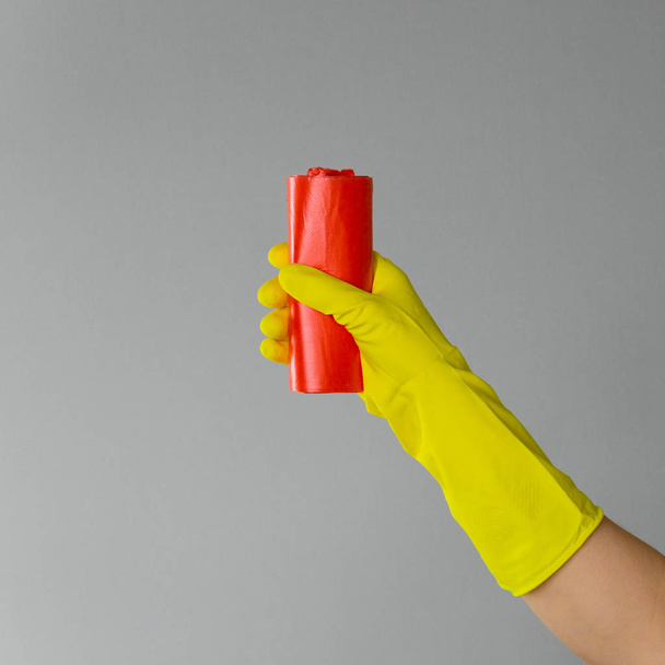 Hand in rubber glove holds colored garbage bag on neutral background. The concept of bright spring, spring cleaning. - Fotó, kép