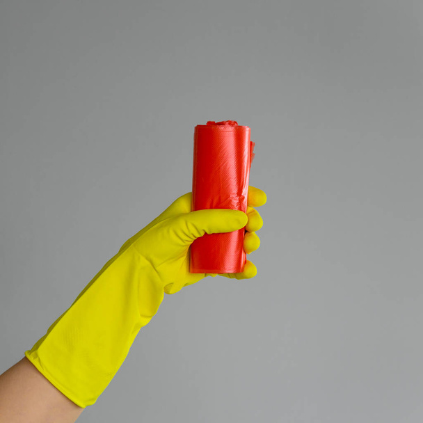 Hand in rubber glove holds colored garbage bag on neutral background. The concept of bright spring, spring cleaning. - Φωτογραφία, εικόνα