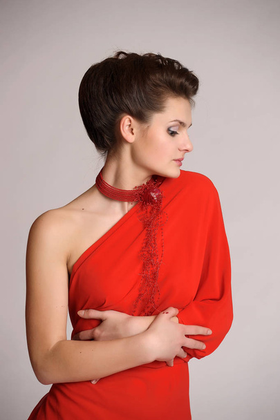 beautiful young brunette in red with a necklace on her neck on a white studio background - Fotó, kép