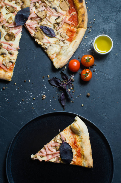 ein Stück frisch gebackene italienische Pizza auf einem schwarzen Teller. dunkler Hintergrund, Draufsicht - Foto, Bild