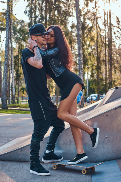 Stylish loving couple enjoying spending time together in the skatepark at the summertime - Photo, Image