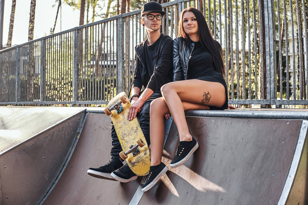 Pareja enamorada sentados juntos en una rampa en el parque de skate en el verano
 - Foto, Imagen