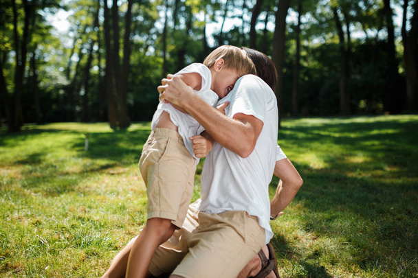 Little blond boy and his father having fun and laughing on the green fresh grass in the open air. - Foto, Imagen