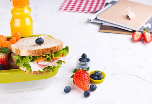Box with school lunch and a bottle of juice. Cheese and lettuce sandwich, fresh berries for baby food and books. Light background and space for text. Copy space. - Foto, Imagem