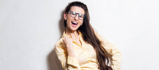 Sí, sí. Retrato de una joven excitada y gritando sobre fondo blanco del estudio. Usar jeans azules, gafas y camisa amarilla
. - Foto, imagen