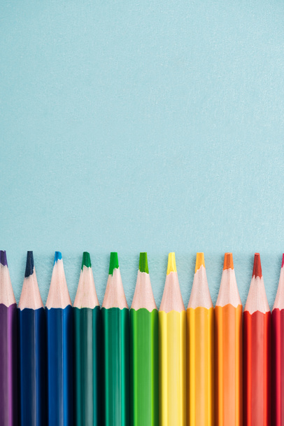top view of rainbow multicolored pencils arranged in horizontal line on blue background, lgbt concept - Fotó, kép