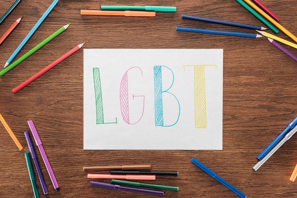 white paper with handwritten word "lgbt", color pencils and felt pens on wooden brown surface - Foto, immagini