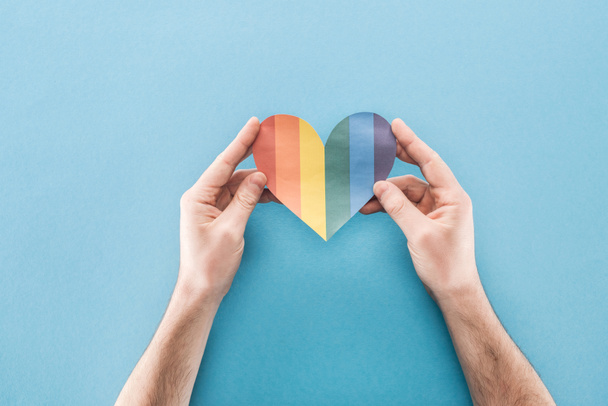 cropped view of male hands with rainbow colored paper heart on blue background, lgbt concept - Foto, Imagem