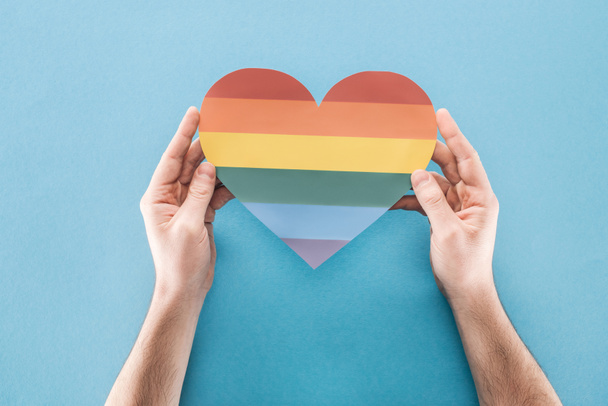 partial view of man holding rainbow colored paper heart on blue background, lgbt concept - Photo, Image