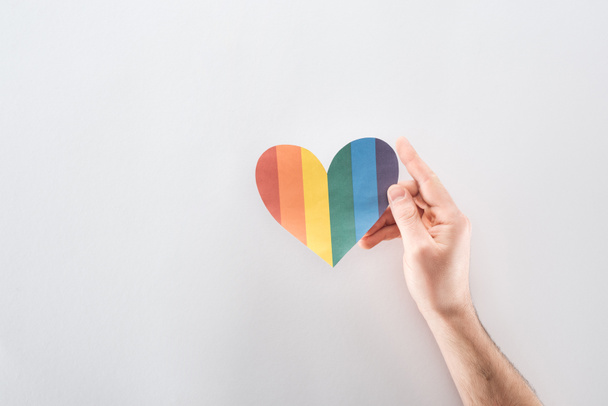 cropped view of male hand with rainbow colored paper heart on grey background, lgbt concept - Foto, Imagem