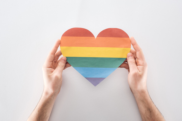 partial view of man holding paper rainbow colored paper heart on grey background, lgbt concept - Foto, imagen