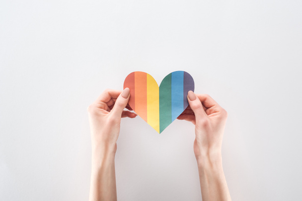 partial view of woman holding rainbow colored paper heart on grey background, lgbt concept - Foto, afbeelding