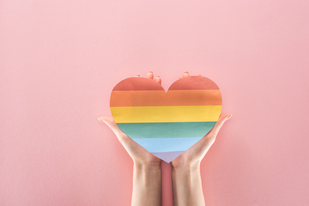 partial view of woman holding rainbow colored paper heart on pink background, lgbt concept - Foto, immagini