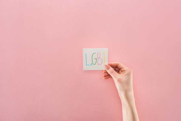 partial view of female hand with "lgbt" handwritten abbreviation on white card on pink background - Foto, imagen