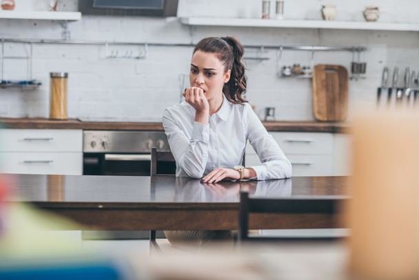 mujer molesta en blusa blanca sentado ar mesa y morder las uñas en la cocina, concepto de trastorno de duelo
 - Foto, Imagen