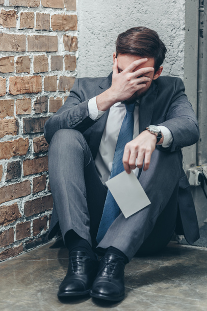 man in grey suit sitting on floor, holding photo and crying on brown textured background in room, grieving disorder concept - Photo, Image