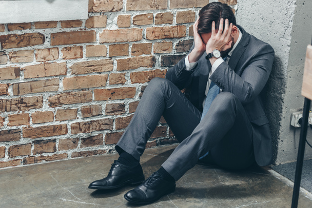 Trauriger Mann im grauen Anzug sitzt in der Ecke auf dem Boden und weint auf strukturiertem Hintergrund im Raum, Konzept der Trauerstörung - Foto, Bild